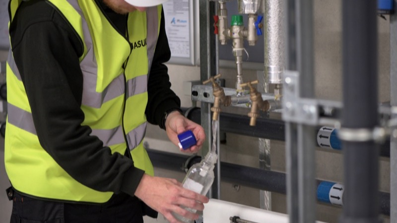 Engineer in hi-vis taking a water sample from pipework